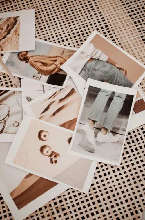 Assorted printed photographs scattered on a woven mat, featuring images of a person, clothing details, and accessories in warm sepia tones.