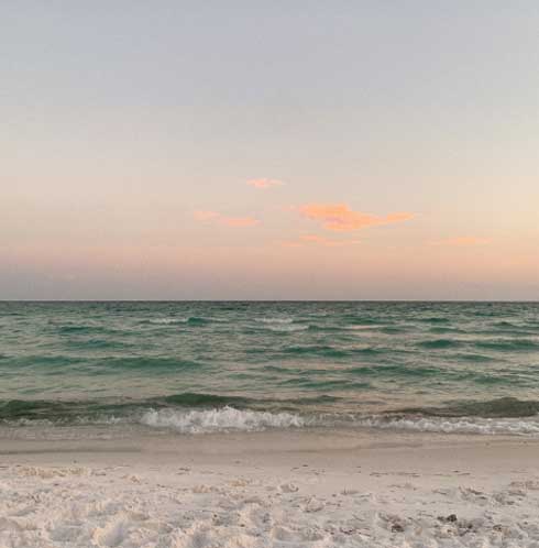 The image shows a tranquil beach scene at dusk with gentle waves lapping onto white sand under a soft gradient sky with hints of pink clouds.