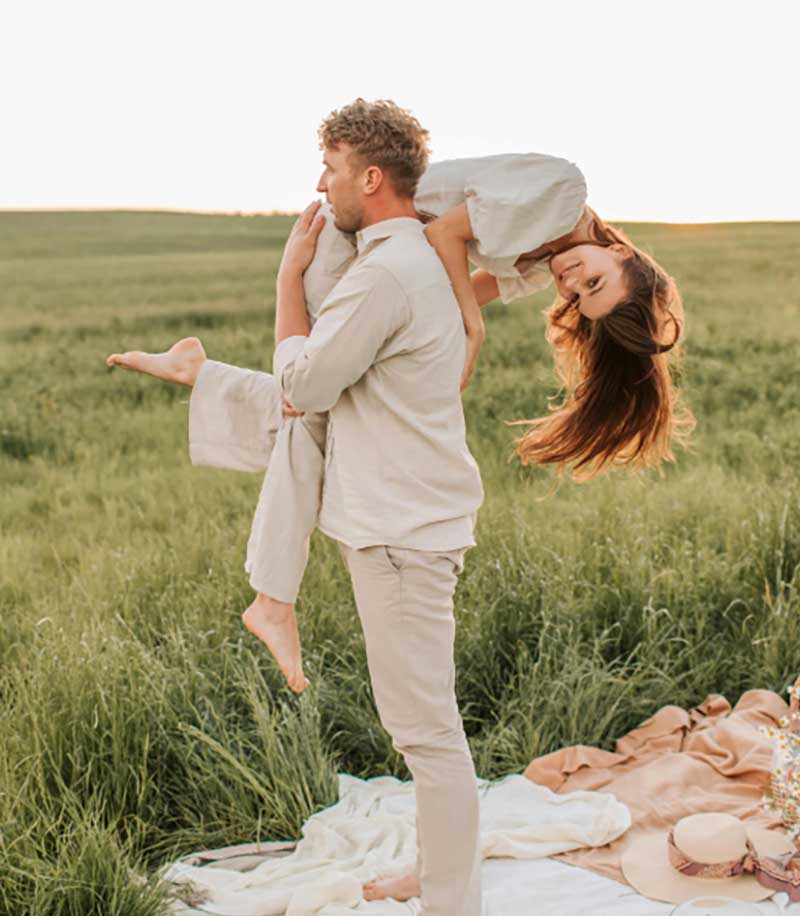 Two people are outdoors in a field. One person is playfully carrying the other on their back, both appearing happy and relaxed.