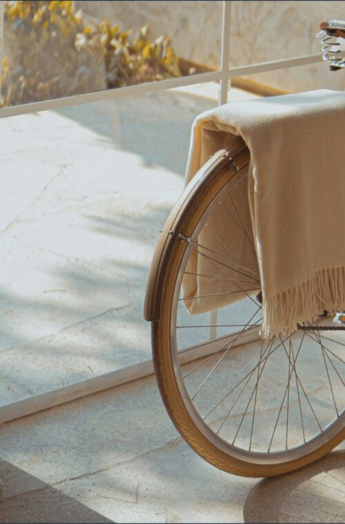 A vintage bicycle rests on a sunny, tiled balcony beside sheer curtains, with a beige blanket draped over its saddle, evoking a serene atmosphere.