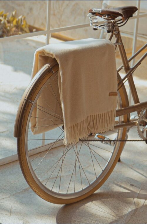 A vintage bicycle rests on a sunny, tiled balcony beside sheer curtains, with a beige blanket draped over its saddle, evoking a serene atmosphere.