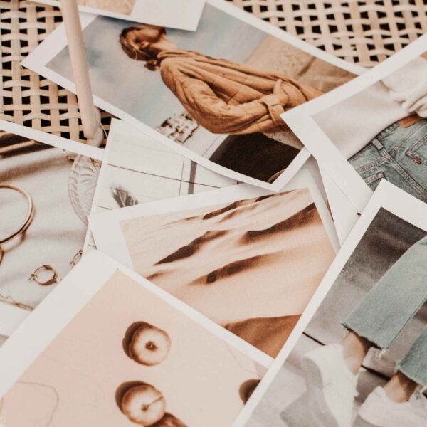 A collection of printed photographs is scattered, showcasing various subjects, including a person, fashion items, and body parts, with a soft color palette.