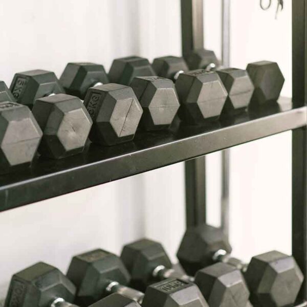 A set of hexagonal black dumbbells neatly arranged on two tiers of a metal rack with a jump rope hanging on the right side.