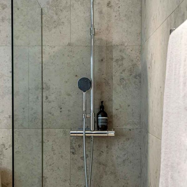 This image shows a modern shower with a stainless steel adjustable showerhead and a single bottle of bathing product placed on a holder.