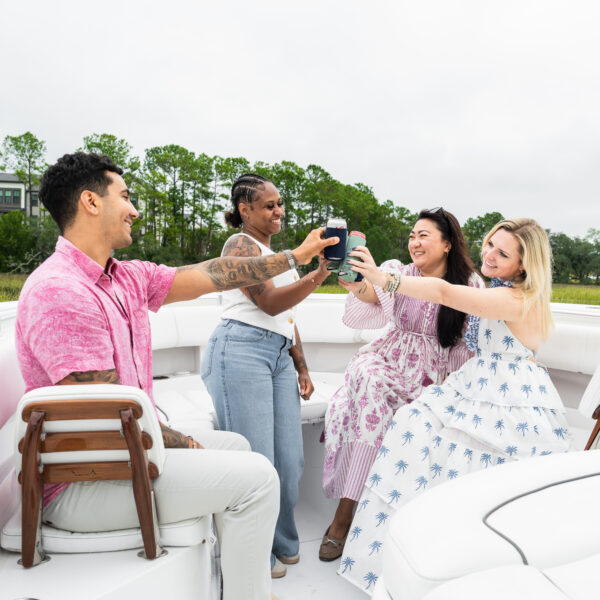 Group of friends relaxing on a boat in Nowell Creek, surrounded by peaceful marshland and coastal scenery.