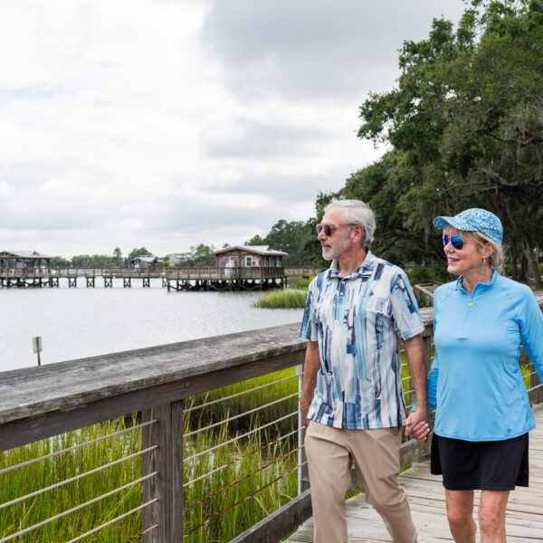 Couple walking along the scenic Daniel Island trail surrounded by trees, greenery, and waterfront views.
