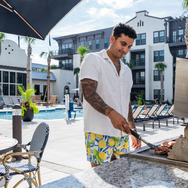 Resident grilling food beside the pool deck at Atlantic Nowell Creek with apartment buildings and palm trees surrounding the courtyard.