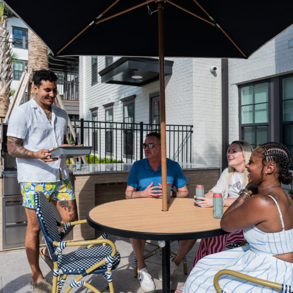 Residents relaxing and talking by the resort-style pool at Atlantic Nowell Creek with lounge chairs and palm trees in the background.