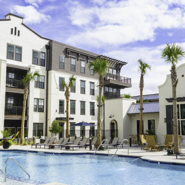 Resort-style pool at Atlantic Nowell Creek featuring lounge chairs, palm trees, and surrounding apartment buildings under a bright Charleston sky.