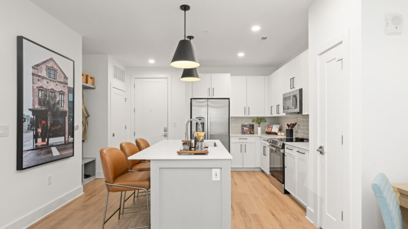 Modern kitchen with white cabinets, stainless steel appliances, a large center island, and two black pendant lights above.