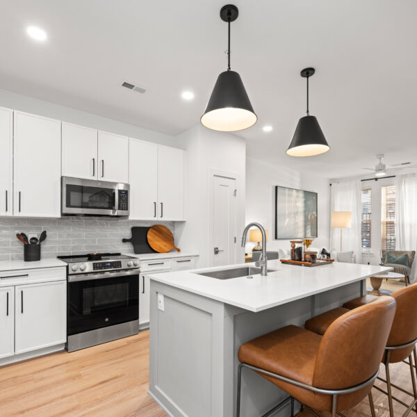 Modern kitchen with white cabinets, stainless steel appliances, a large center island, and two black pendant lights above.