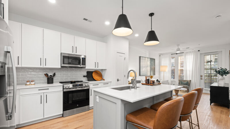 Modern kitchen with white cabinets, stainless steel appliances, a large center island, and two black pendant lights above.