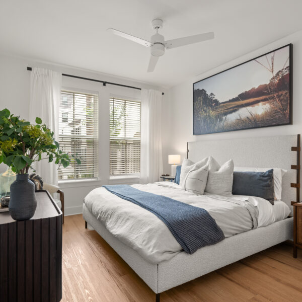 Bright bedroom featuring white bedding, two bedside tables with lamps, and a window with white curtains.