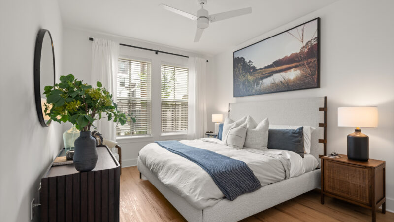 Bright bedroom featuring white bedding, two bedside tables with lamps, and a window with white curtains.