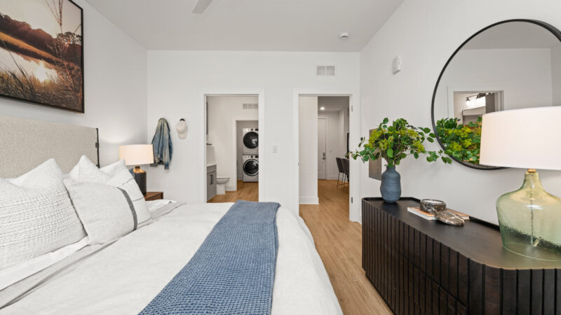 Modern bedroom with a textured headboard, woven nightstand, and large landscape photograph above the bed.