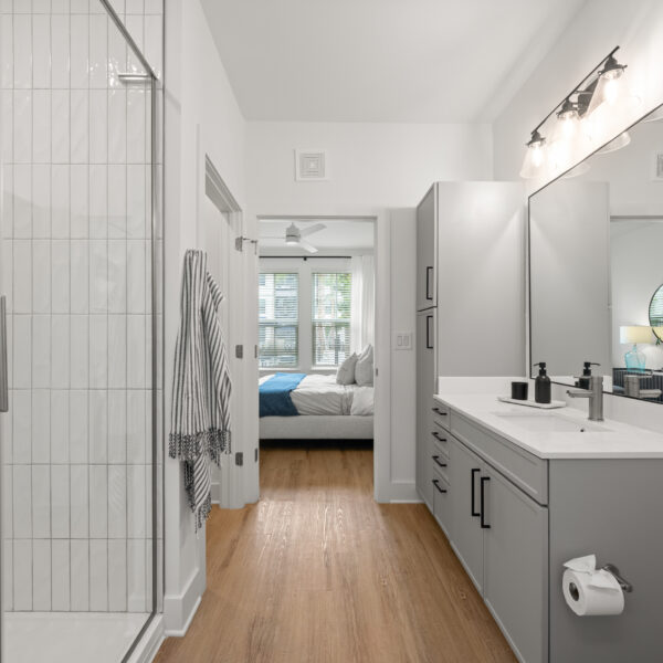 Bright bathroom featuring white tile shower walls, gray cabinetry, and a wide mirror above the sink.