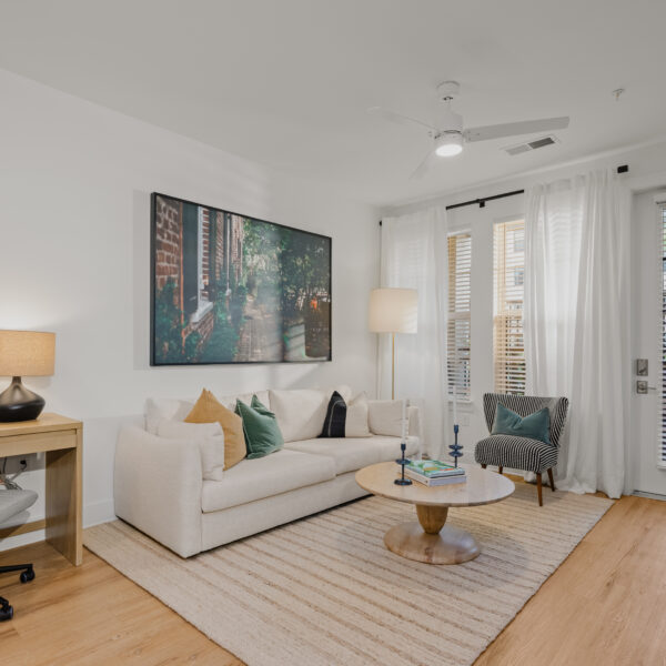 Cozy living room with a white sofa, accent chair, wood coffee table, and large windows with sheer curtains.